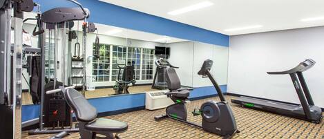 Un gimnasio con equipo de ejercicio, un muro con espejos y un suelo estampado.