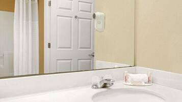 Un baño con lavamanos blanco, un espejo, toallero y cortina de ducha.