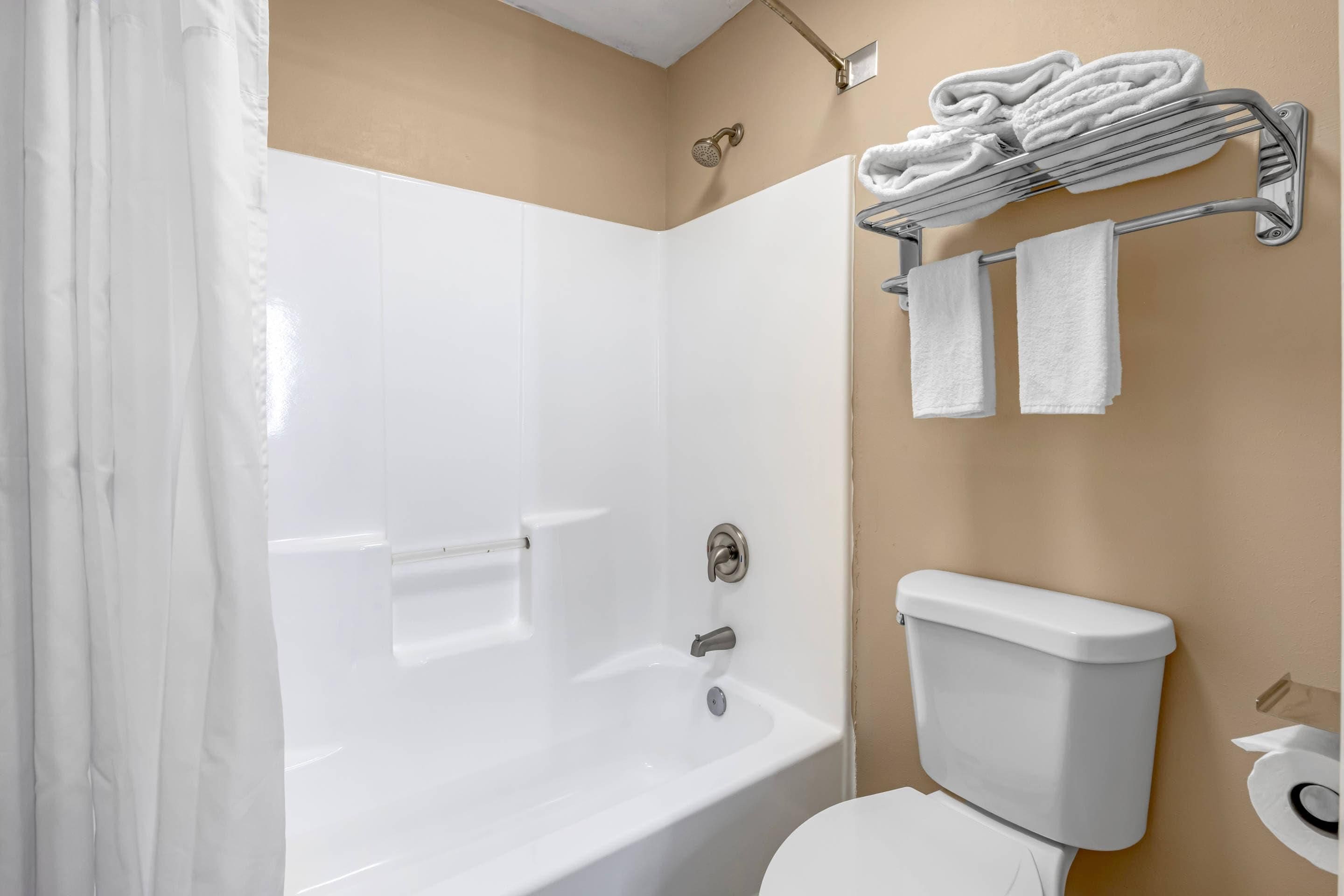 A bathroom with a white bathtub, a toilet, and a towel rack with folded towels.