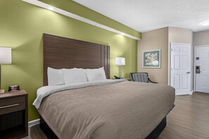 A hotel room with a large bed, bedside tables, a lamp, a chair, and a door. - Quality Inn Ormond Beach – Daytona (Ormond Beach)