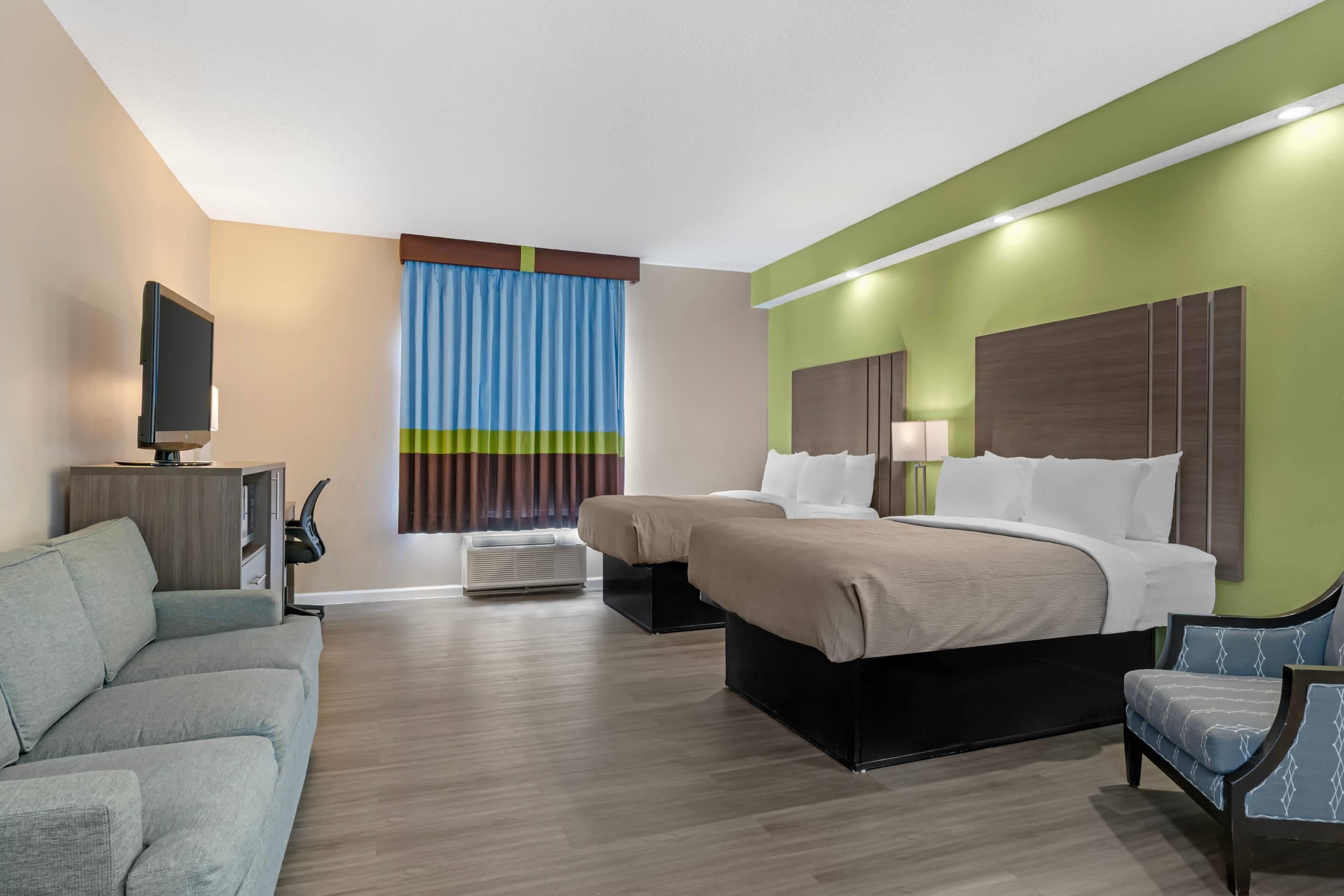 Ein Hotelzimmer mit einem Bett, zwei Nachttischen, einem Schreibtisch mit Stuhl, einem Fernseher und einem Fenster mit Vorhängen.