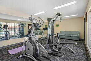 A gym with cardio equipment, a mirror, and a green couch. - Quality Inn Ormond Beach – Daytona (Ormond Beach)