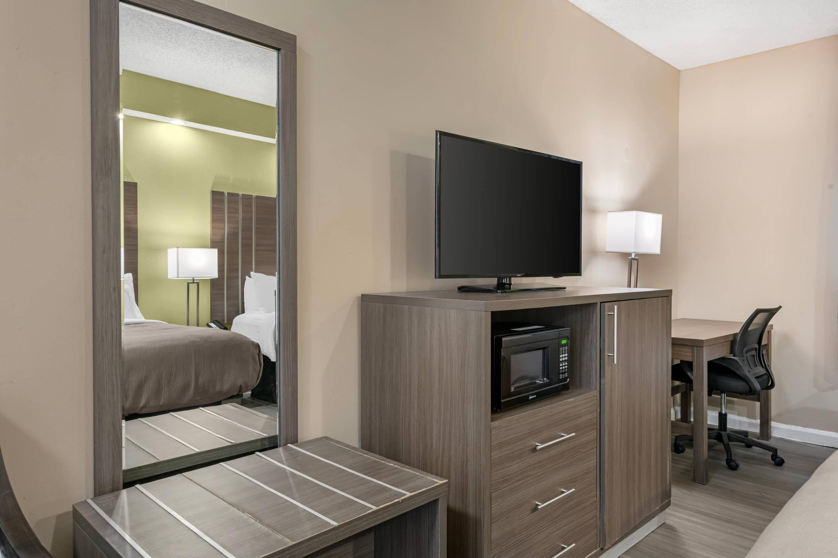 Habitación de hotel con cama, escritorio, televisor de pantalla plana, microondas, silla y lámpara.