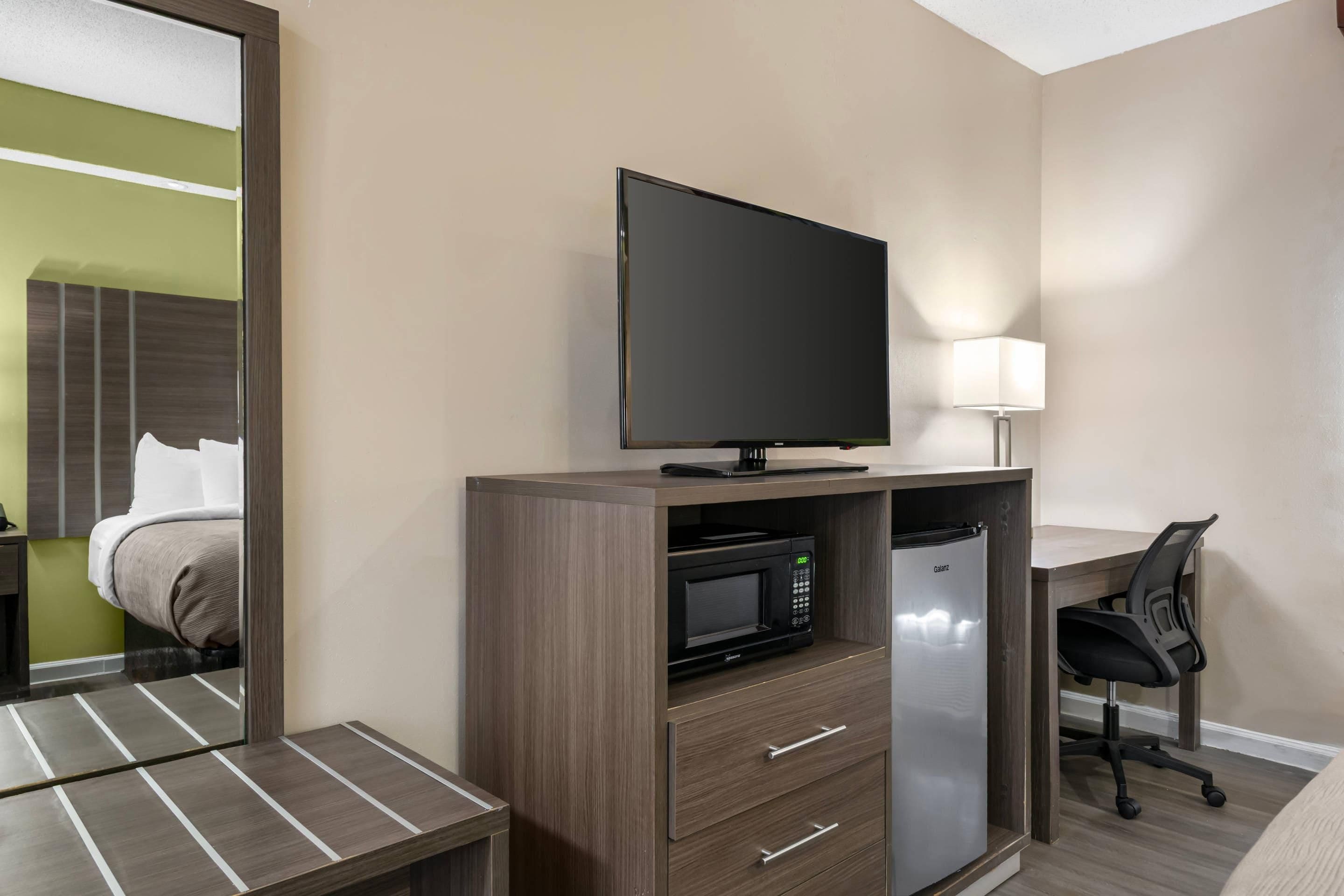 A hotel room with a bed, a desk with a chair, a television, a microwave, and a refrigerator.