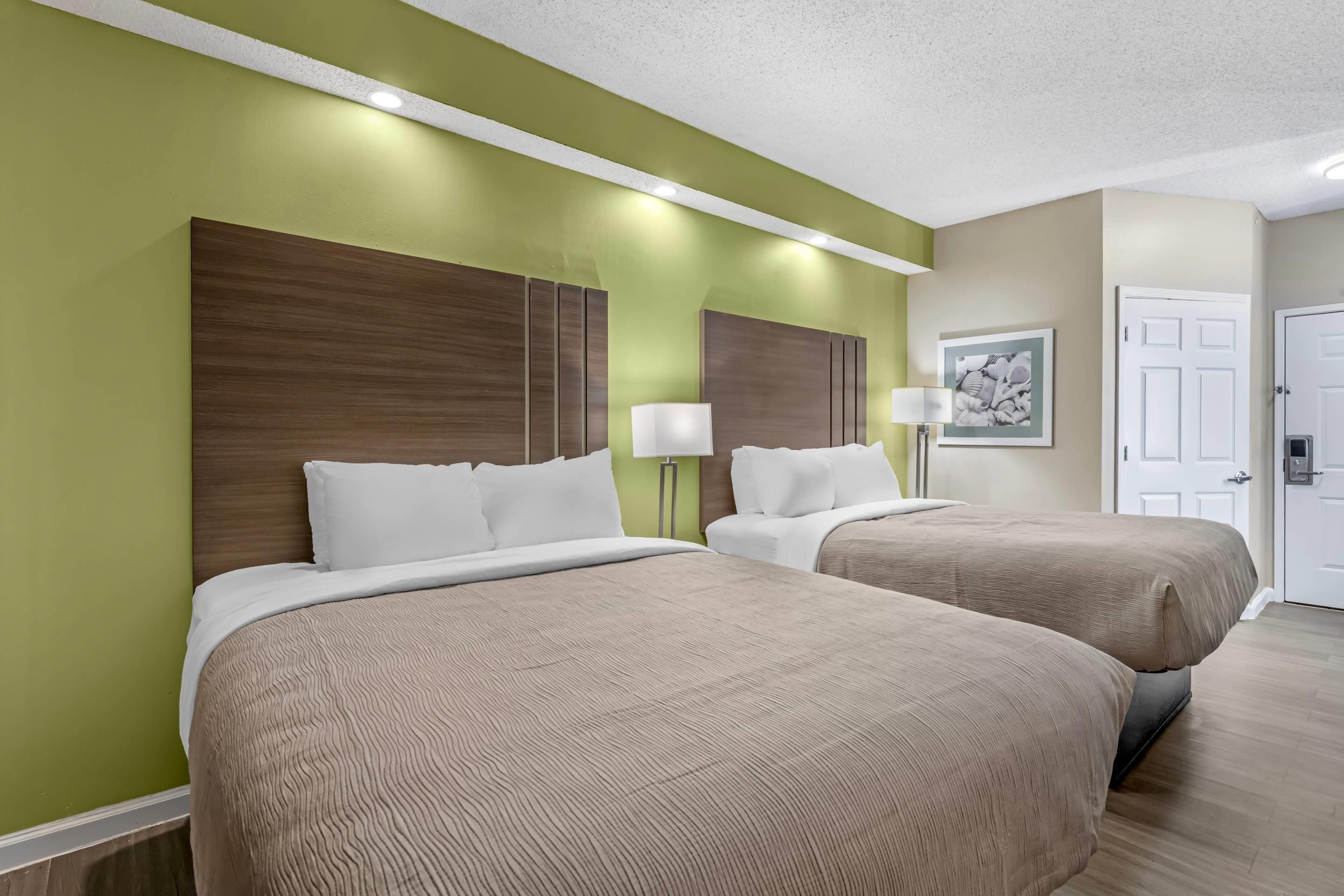 Une chambre d’hôtel avec deux lits, un mur vert et une porte.