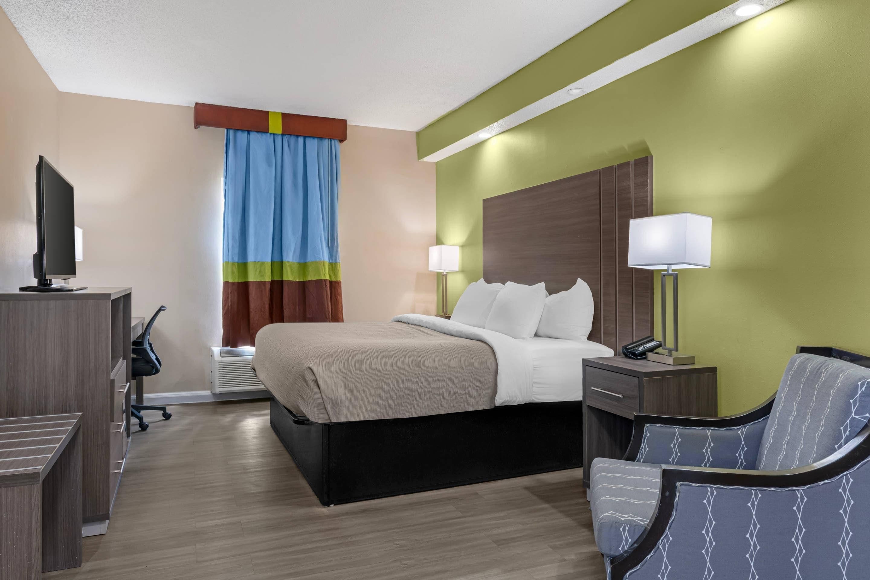 Una camera d'albergo con un letto, lampade sui comodini, una scrivania con un computer, una sedia e una televisione.
