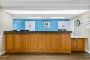 A reception desk with a blue wall, a sign for 'Quality by Choice Hotels,' and a clock on the wall. - Quality Inn Ormond Beach – Daytona (Ormond Beach)