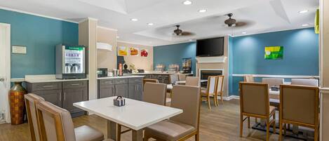 A modern kitchen with a dining area, equipped with a refrigerator, microwave, and a flat-screen TV.