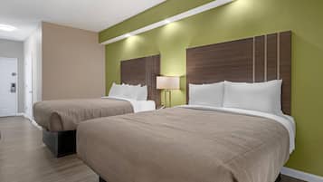 Een hotelkamer met twee bedden, een nachtkastje met een lamp en een deur.