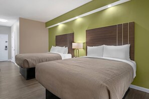 A hotel room with two beds, a nightstand with a lamp, and a door.