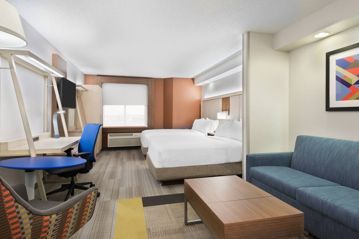 A hotel room with a bed, a desk, a chair, a sofa, and a TV.