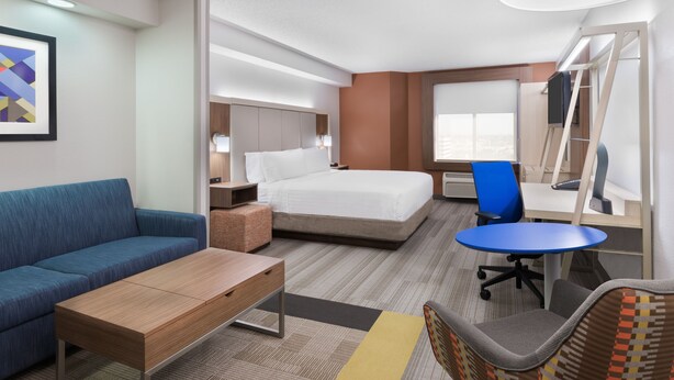 A hotel room with a bed, a sofa, a desk, a chair, a lamp, and a window. - Holiday Inn Express & Suites Nearest Universal Orlando by IHG (Orlando)