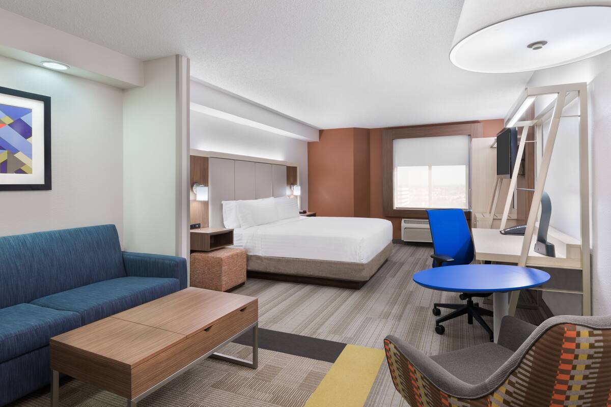 A hotel room with a bed, a sofa, a desk, a chair, a lamp, and a window.