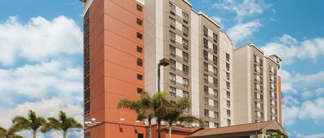 A multi-story hotel with a flat roof, a prominent entrance with a covered area, and a white fence surrounding the property.