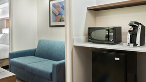 A hotel room with a blue sofa, a microwave, a coffee machine, and a small refrigerator. - Holiday Inn Express & Suites Nearest Universal Orlando by IHG (Orlando)