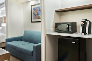 A hotel room with a blue sofa, a microwave, a coffee machine, and a small refrigerator.
