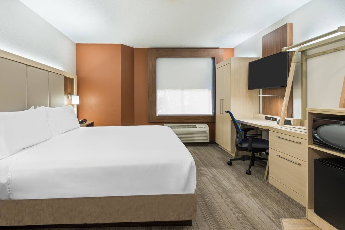 A hotel room with a large bed, a desk with a chair, a television, and a wardrobe.