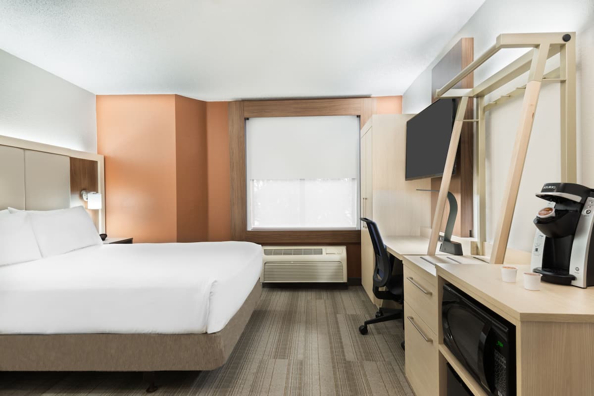 A hotel room with a bed, desk, chair, and a coffee maker.