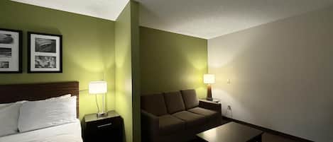 Una habitación de hotel con cama, sofá, una mesita y dos lámparas.