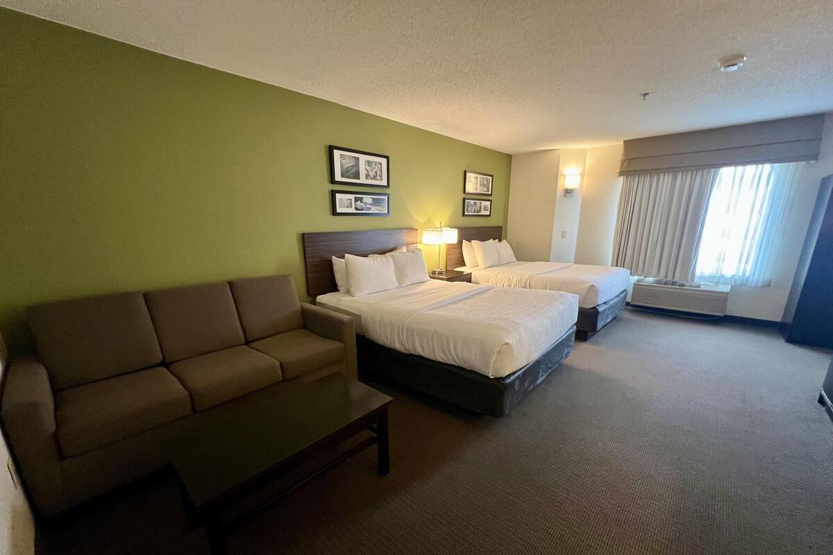 A hotel room with two beds, a sofa, a small table, and a window with curtains.