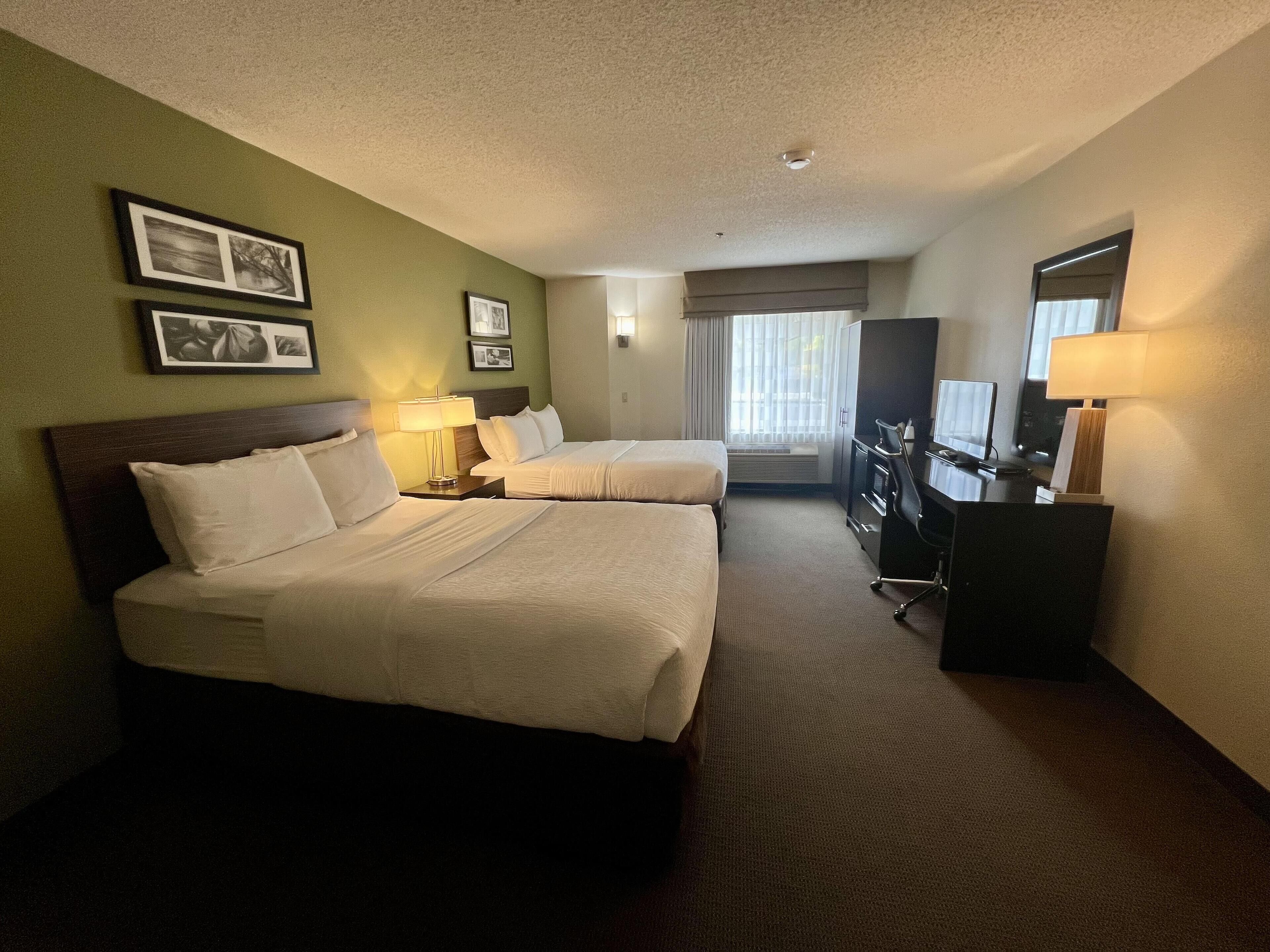 Une chambre d’hôtel avec deux lits, un bureau, une chaise, une commode et une fenêtre avec des rideaux.