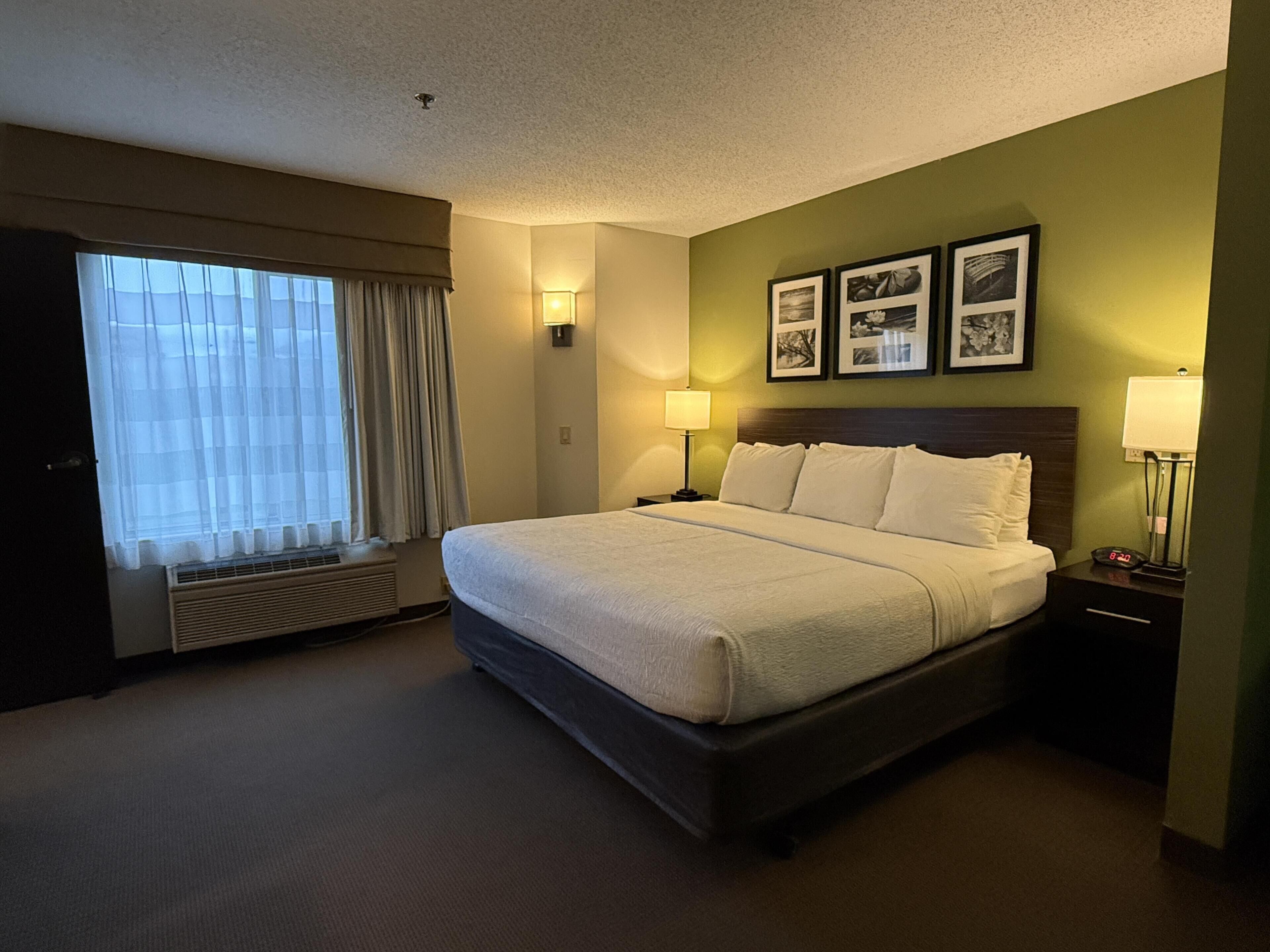 A hotel room with a large bed, two bedside lamps, a wall-mounted clock, and a window with curtains.