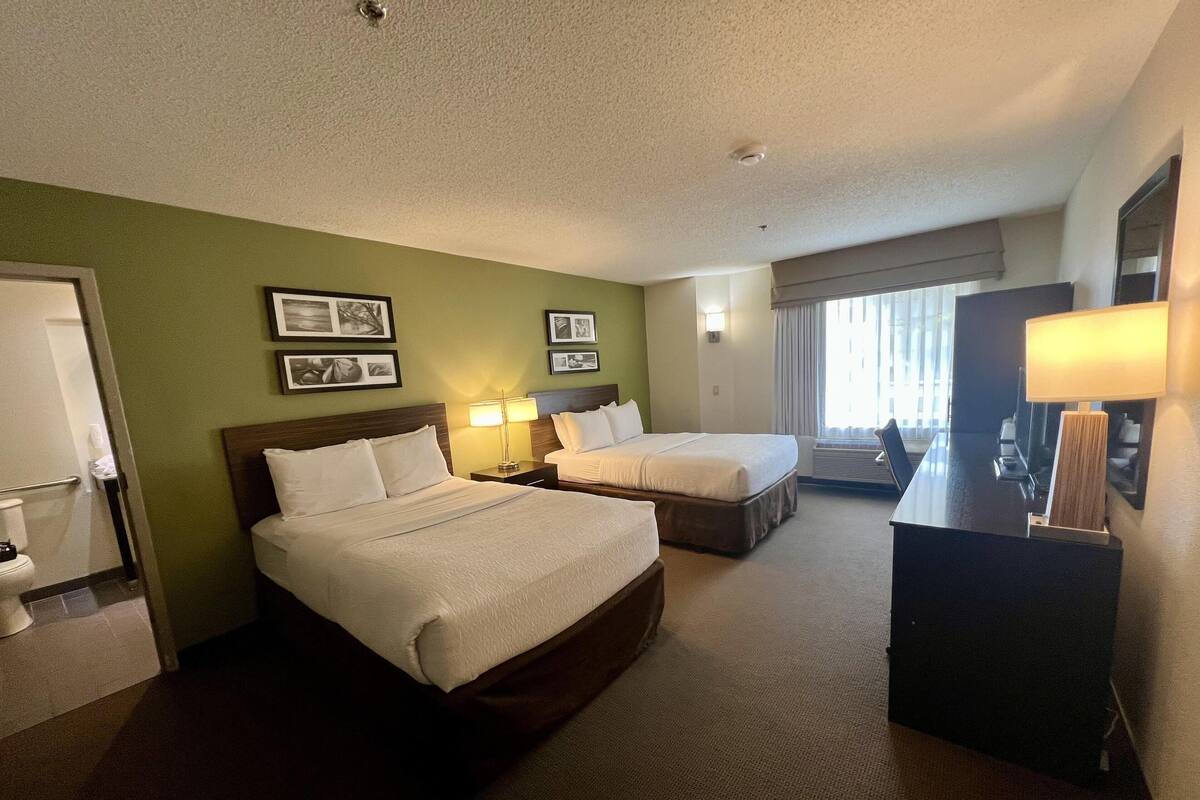 A hotel room with two beds, a desk, and a bathroom.
