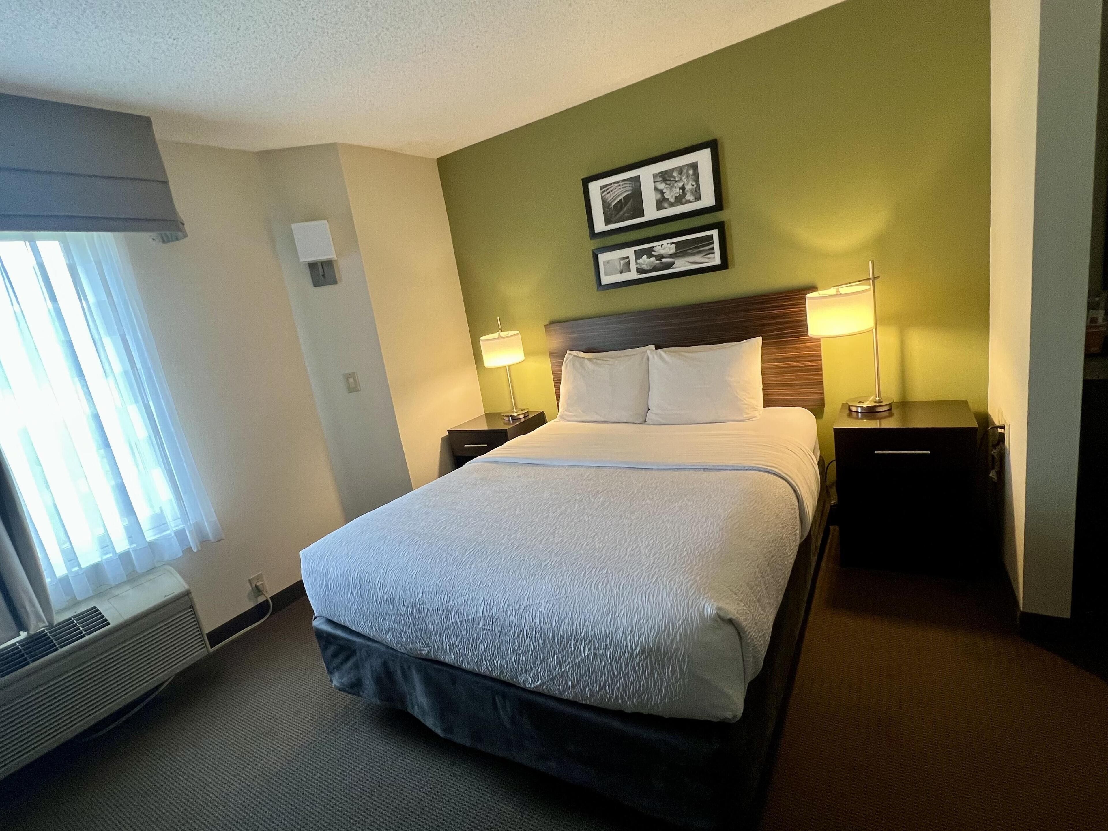 A hotel room with a large bed, two bedside tables with lamps, a wall-mounted picture, and a window with curtains.
