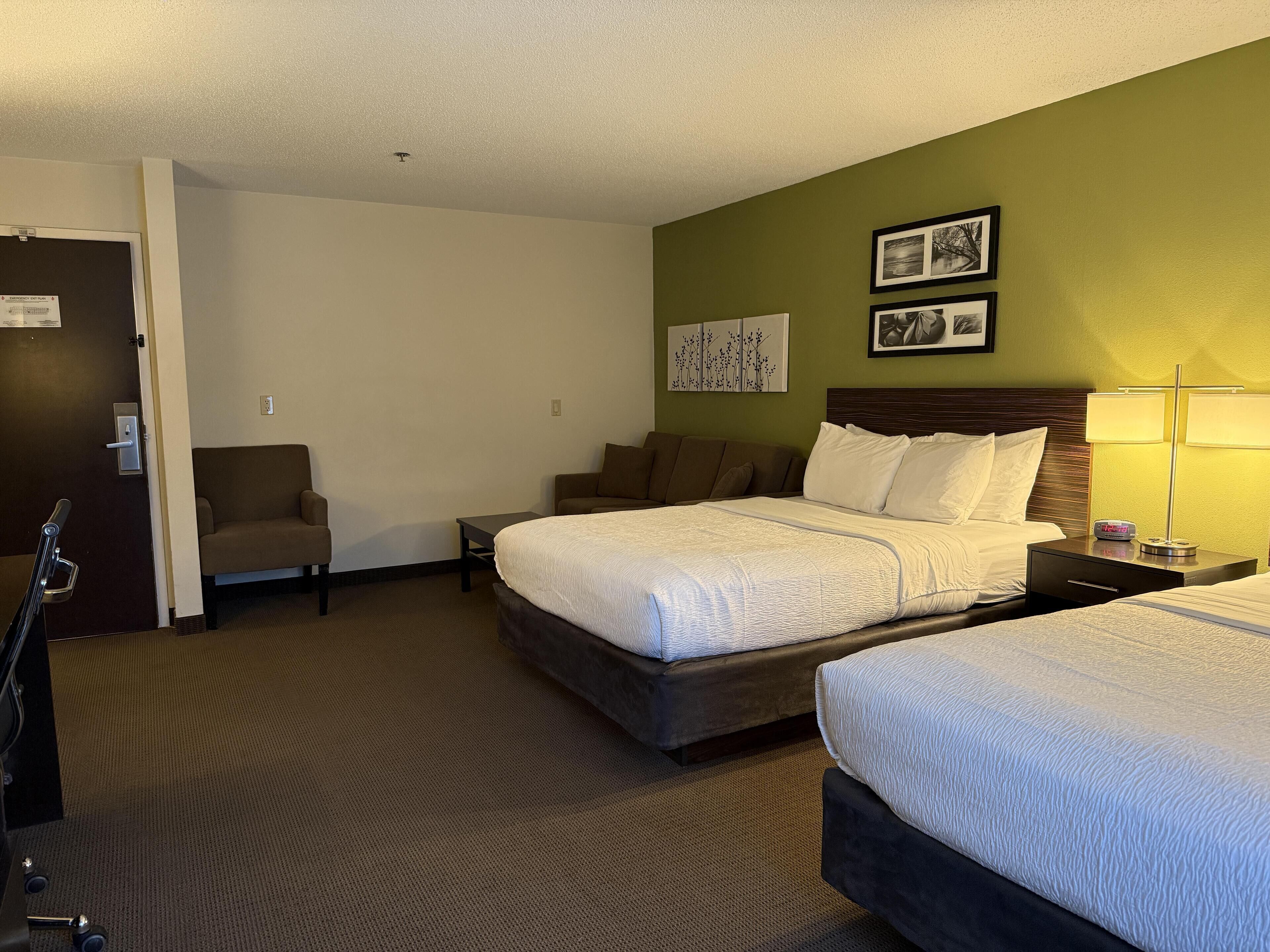 A hotel room with a large bed, a smaller bed, a chair, a desk, and a lamp.
