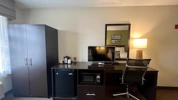 A hotel room with a dark wooden desk, a small refrigerator, a television, a chair, and a bed with a nightstand.