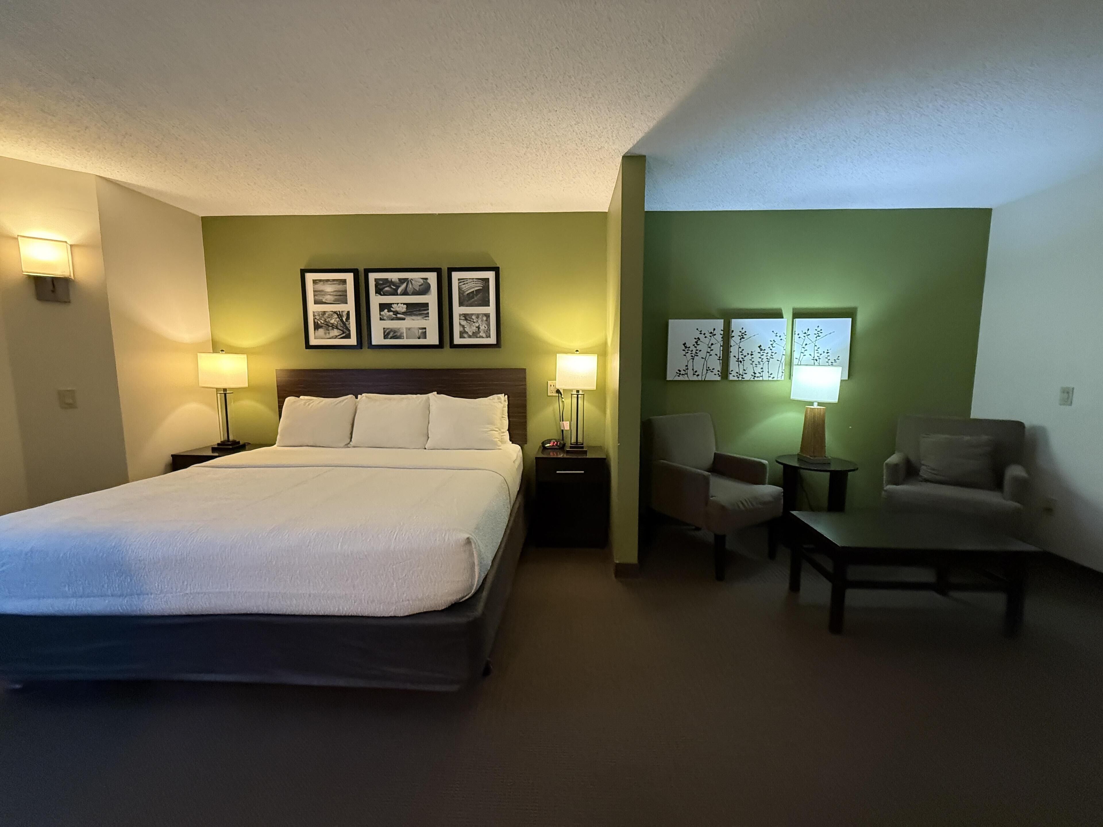 Ein Hotelzimmer mit einem Bett, zwei Sesseln, einem Tisch und Wandleuchten.