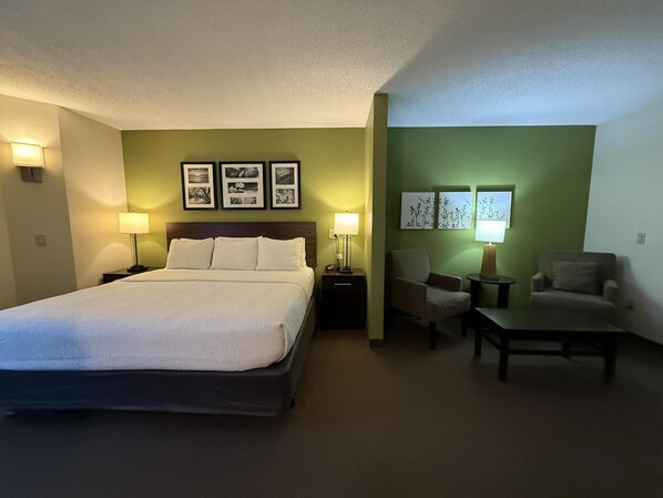 Habitación de hotel con cama, dos sillones, una mesa y lámparas fijadas a la pared.