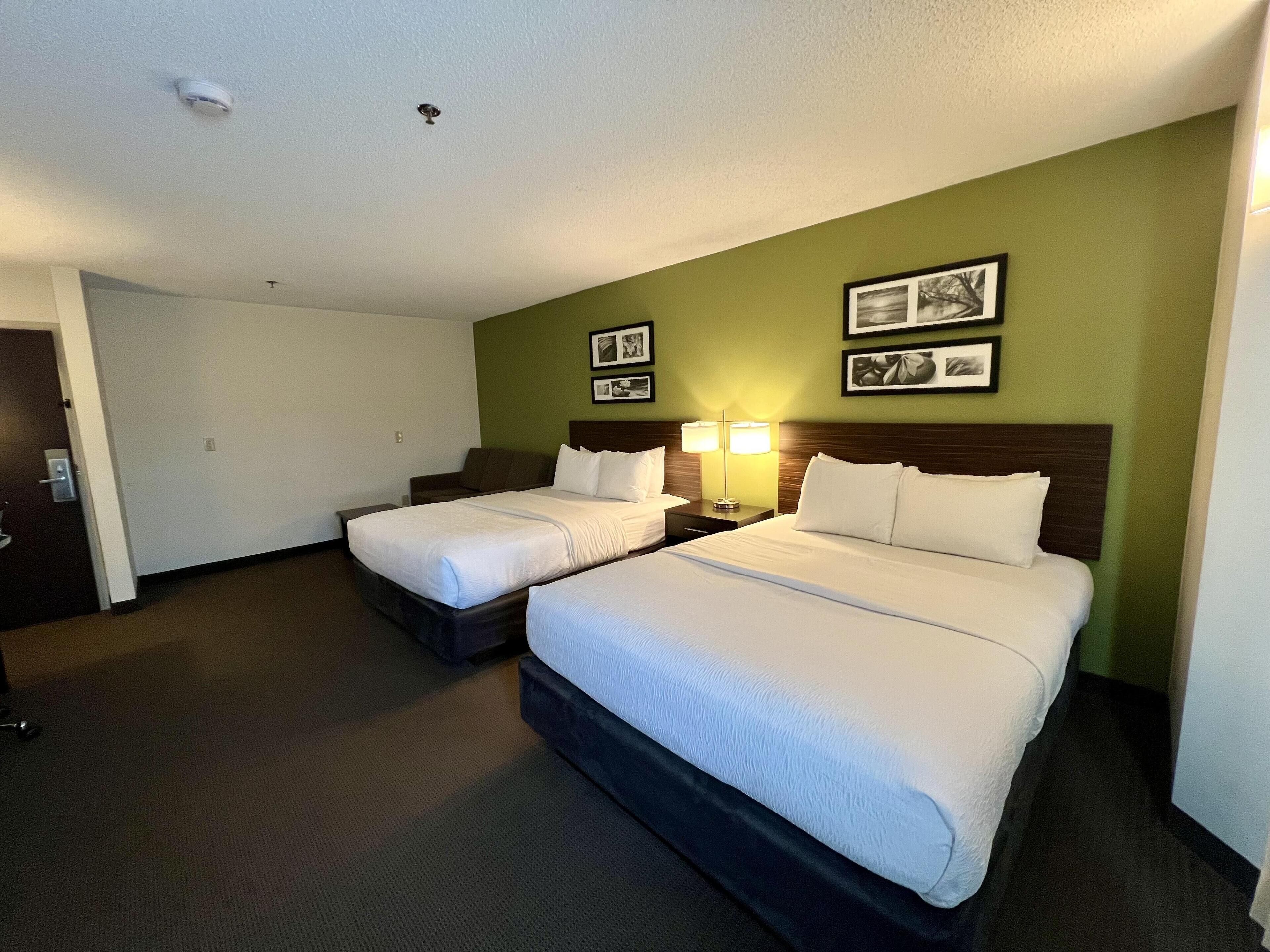 A hotel room with two beds, a desk, a chair, a lamp, and two framed pictures on the wall.