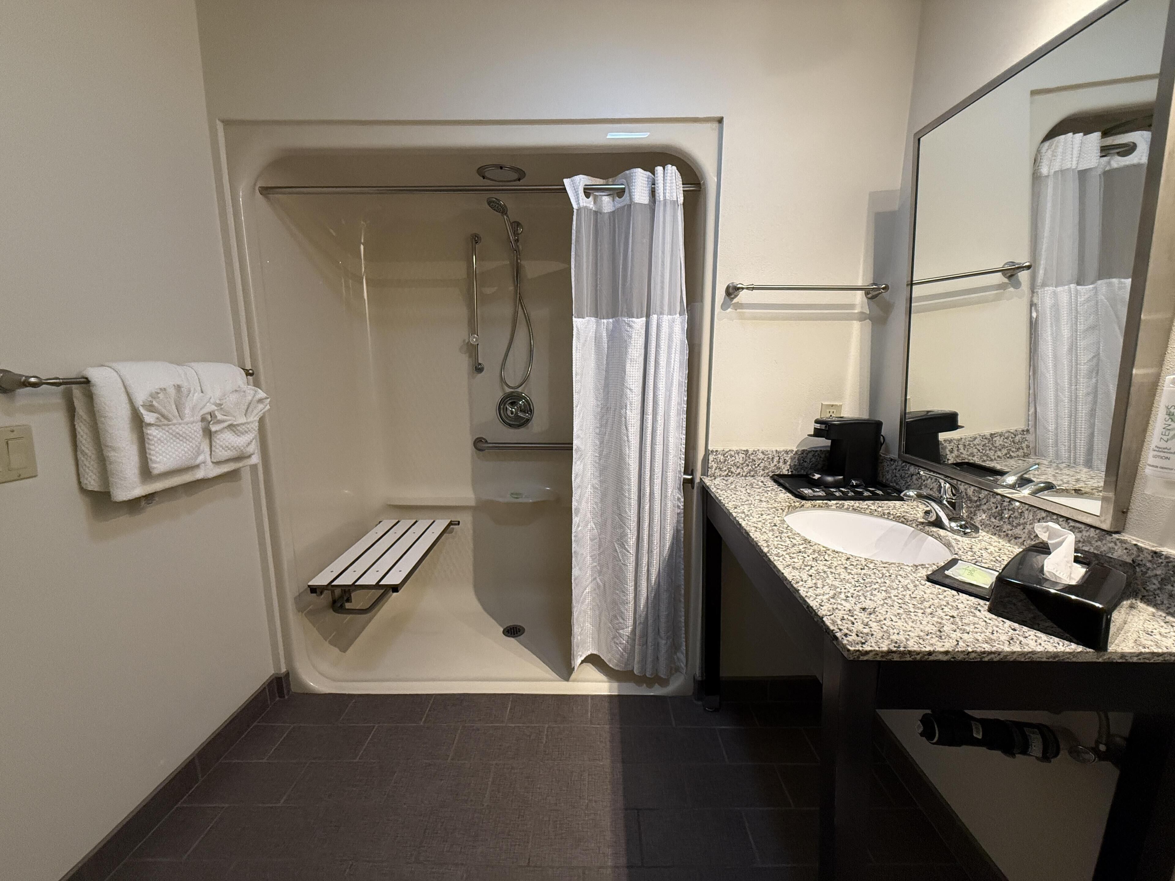 A bathroom with a shower, a sink, a towel rack, and a mirror.