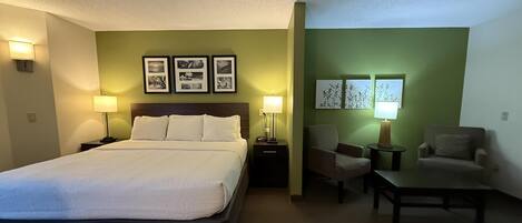 Una habitación de hotel con una cama, dos sillas, una mesita y lámparas fijadas a la pared.