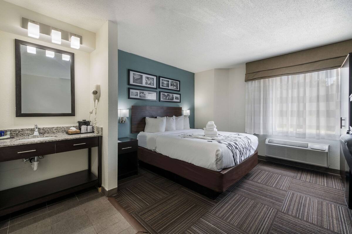 A hotel room with a bed, a vanity with a mirror, and a window with curtains.