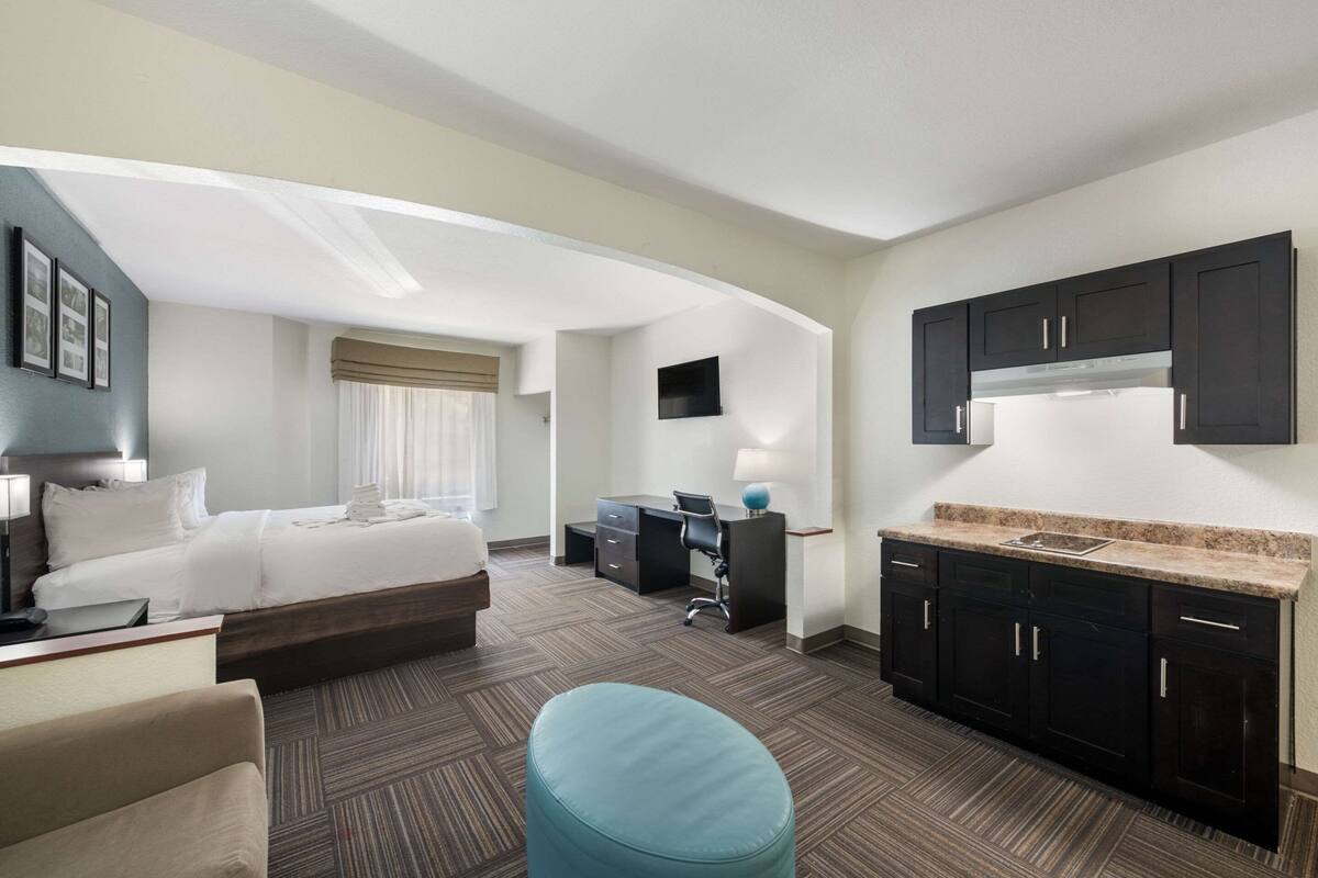 A hotel room with a bed, desk, kitchenette, and a seating area.