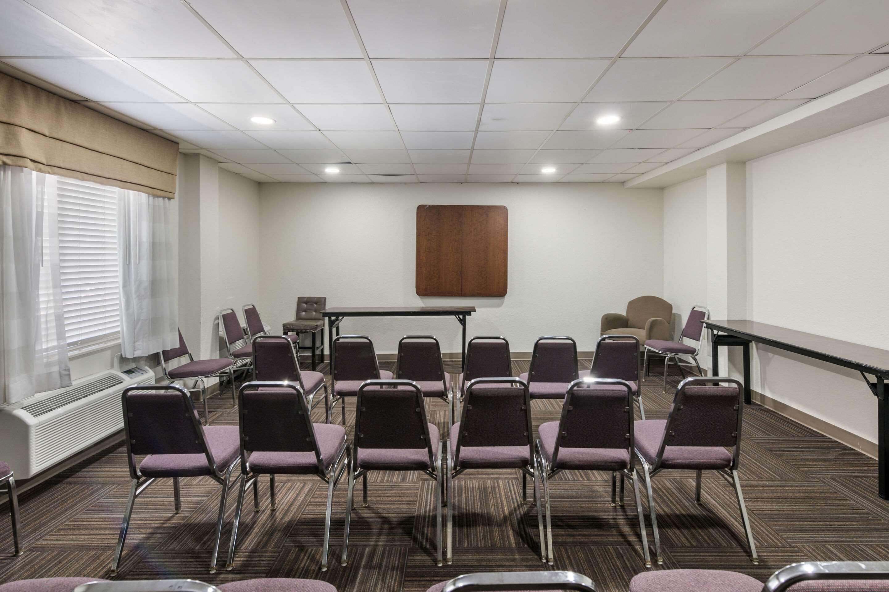 A conference room with a long table, multiple chairs, a projector screen, and a window with blinds.