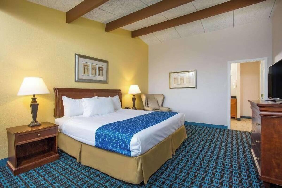 A hotel room with a bed, two bedside lamps, a chair, a desk, and a television.