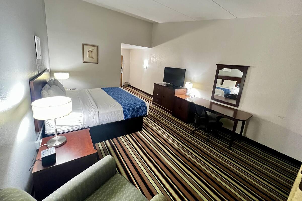 A hotel room with a bed, desk, chair, TV, and a mirror.