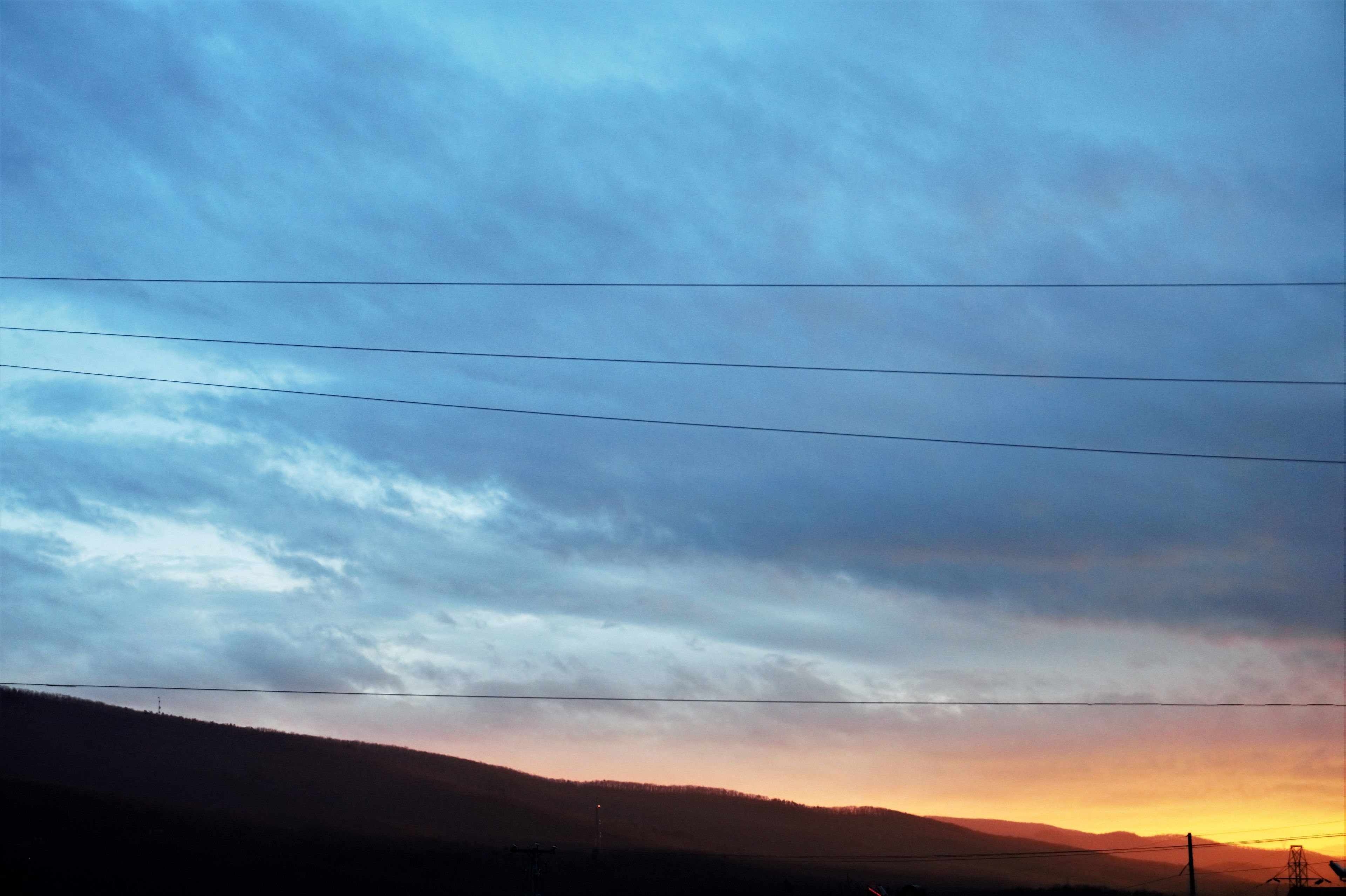A sunset over a hilly landscape with power lines running horizontally across the sky.