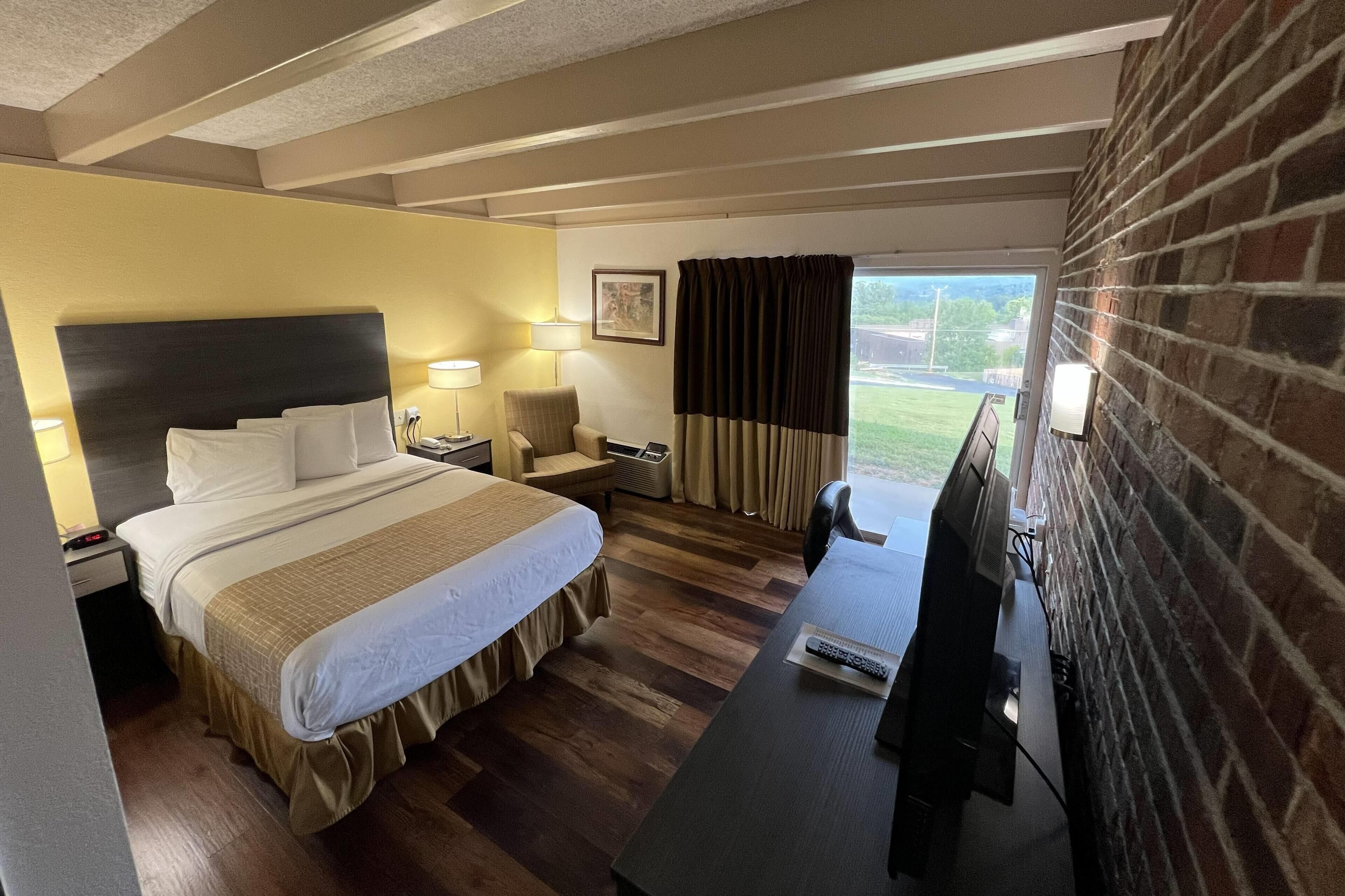Habitación de hotel con cama, mesitas de noche, escritorio, silla, televisión y vistas al exterior.