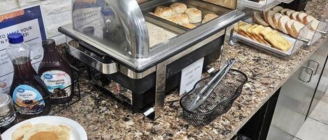 A buffet counter with various food items, including pastries, bread, and a grill station.