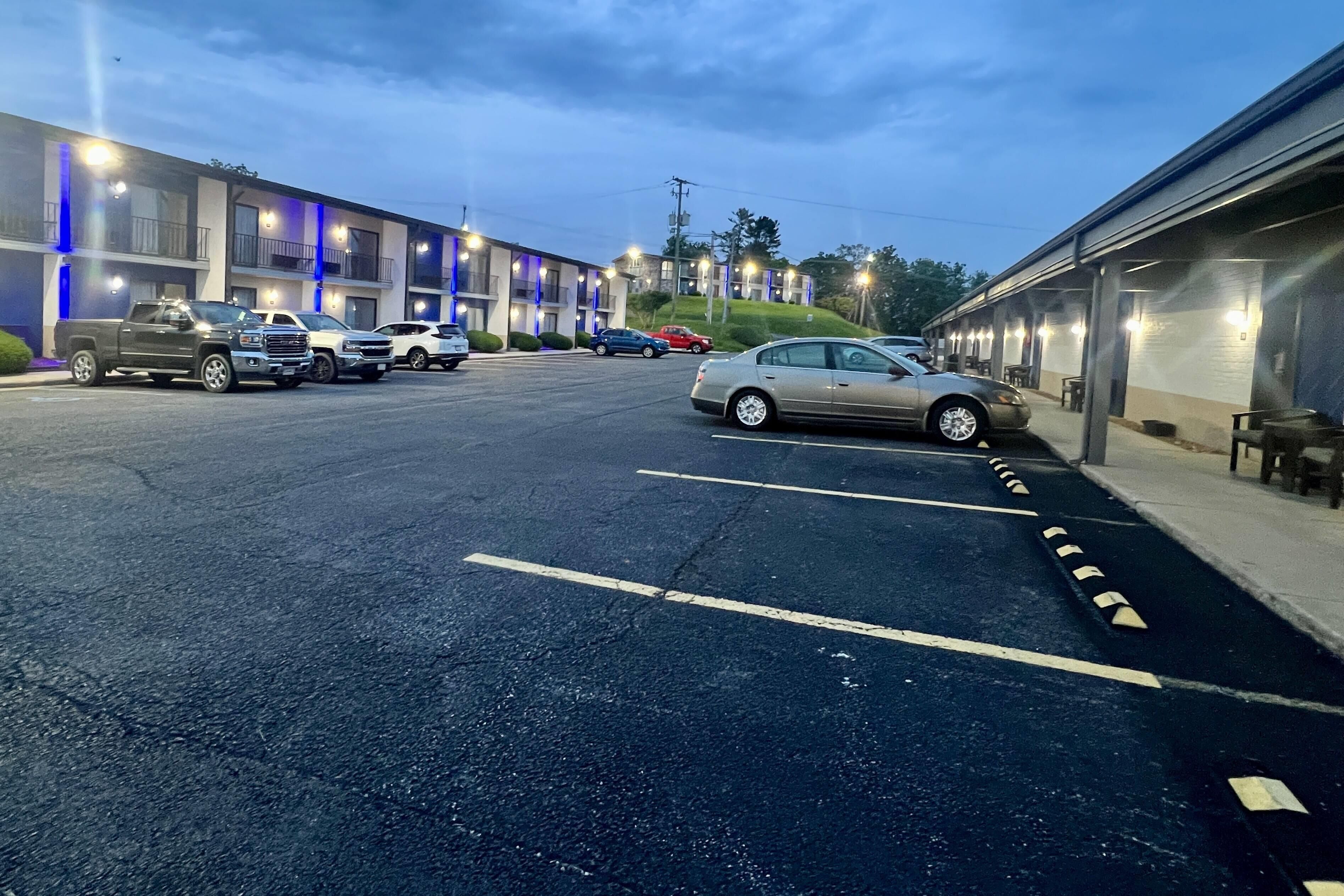 A parking lot with several cars, a building with balconies, and a covered area with tables and chairs.