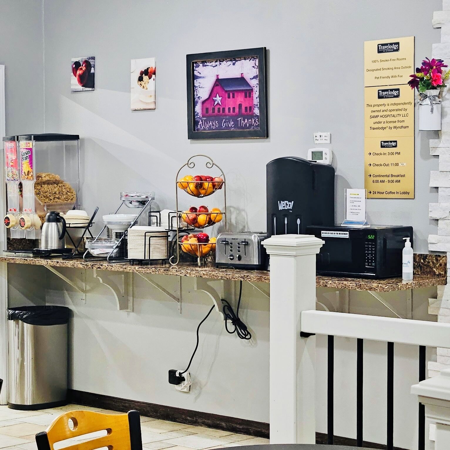 Zona de recepción de un hotel con mostrador, máquina de café, contenedor de basura y un cartel con información sobre los servicios del hotel.