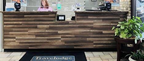 Un mostrador de recepción con detalles de madera, un reloj encima y un cartel que dice 'Travelodge'.