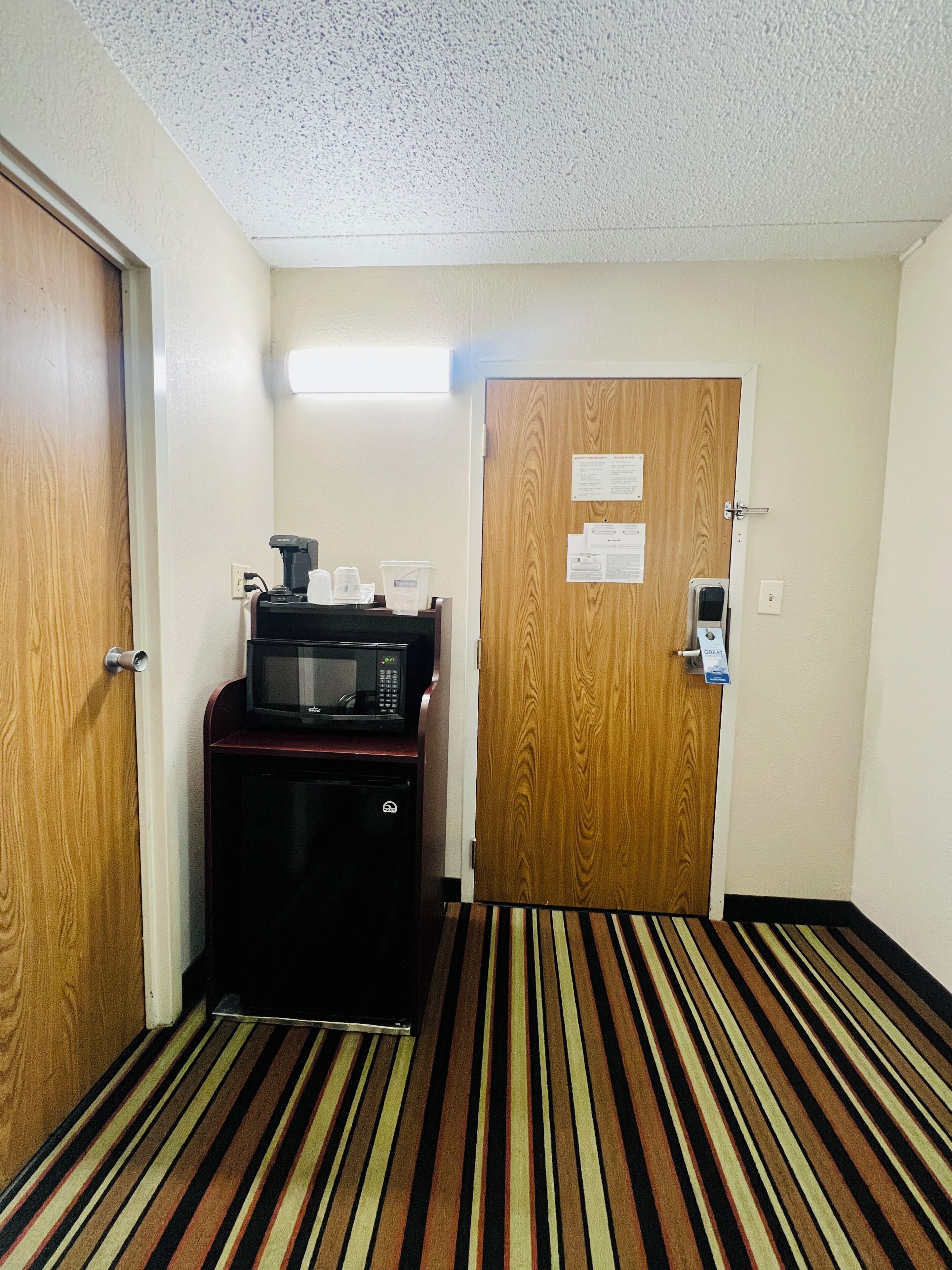 Habitación de hotel con microondas, refrigerador y un cartel identificador en la puerta.