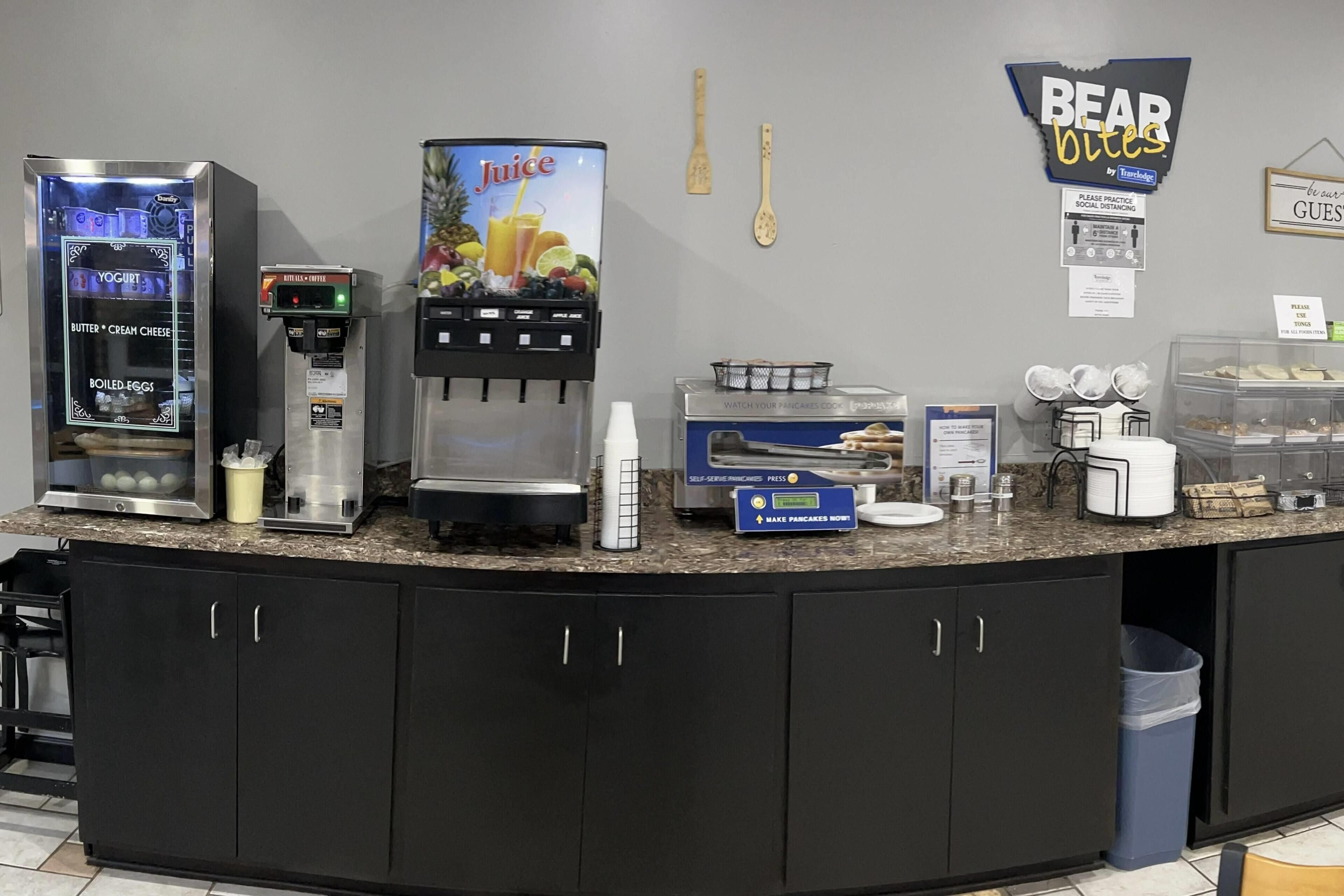 Una barra de desayuno con máquina de yogur, dispensador de zumo, máquina para hacer tortitas de autoservicio y un cartel que pone 'Bear Bites'.