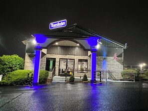Un hotel Travelodge con fachada de ladrillo, entrada amplia y bandera estadounidense.