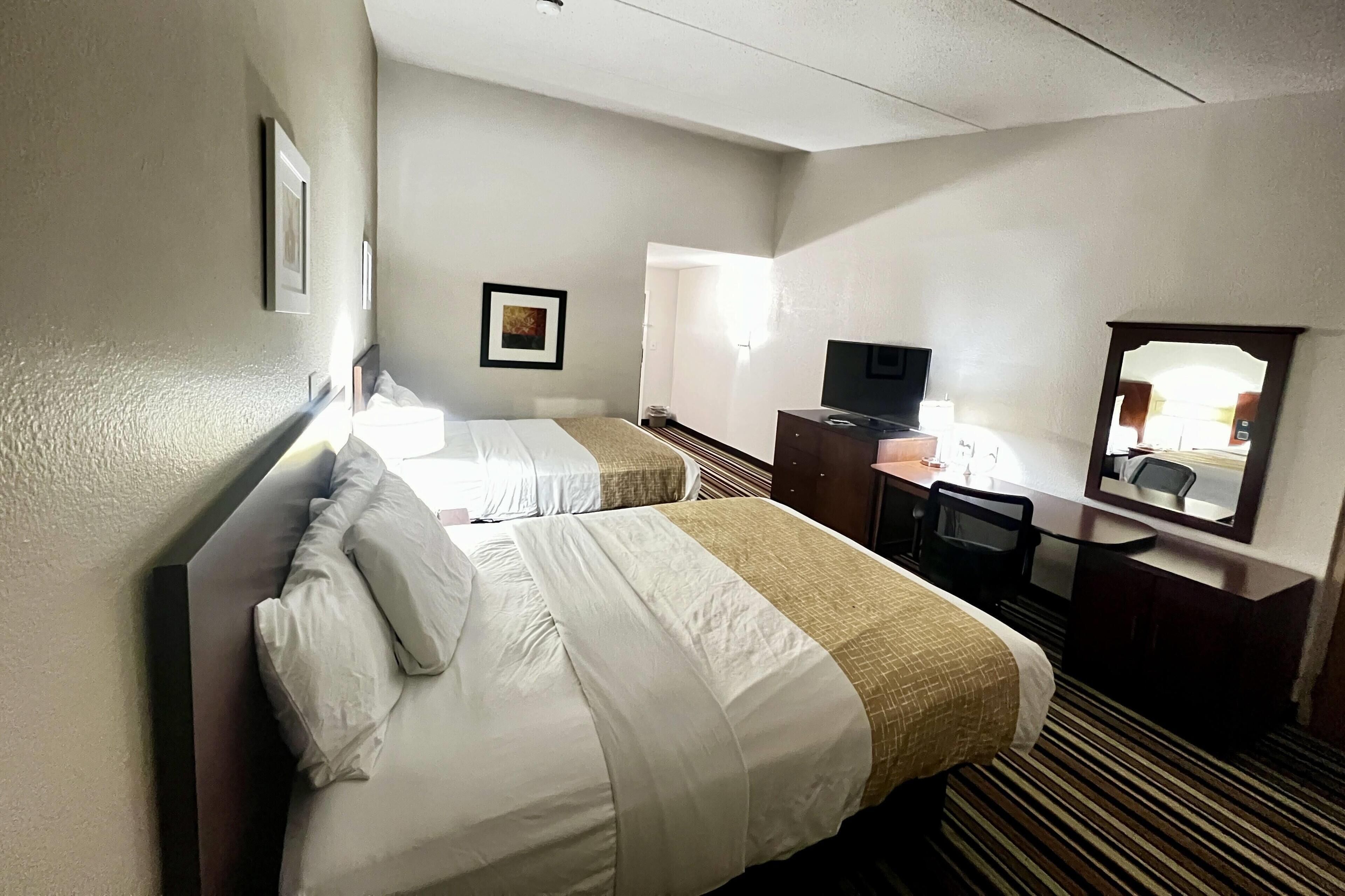 A hotel room with two beds, a desk, a television, and a mirror.